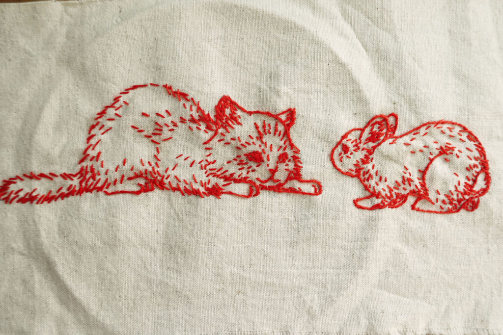 子猫とうさぎが向かい合って、お互いを見ている、赤い糸の刺繍作品
