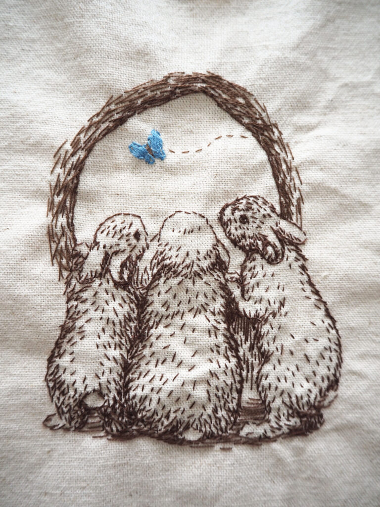飛んできた青い蝶を穴から外を覗く３匹のうさぎ。刺繍作品